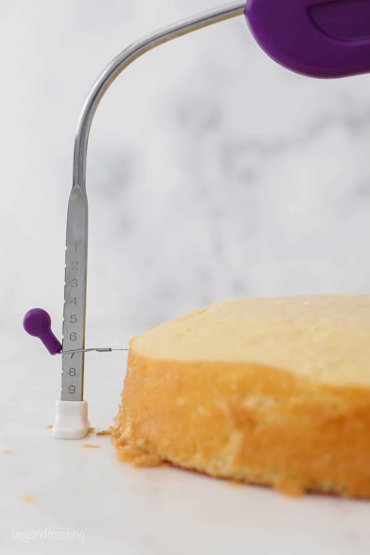 Learn how to make a layer cake with this easy step-by-step tutorial. Everything you need to know, from leveling cakes to frosting the layers! Close up of a cake level trimming the dome from the top of a vanilla cake layer.