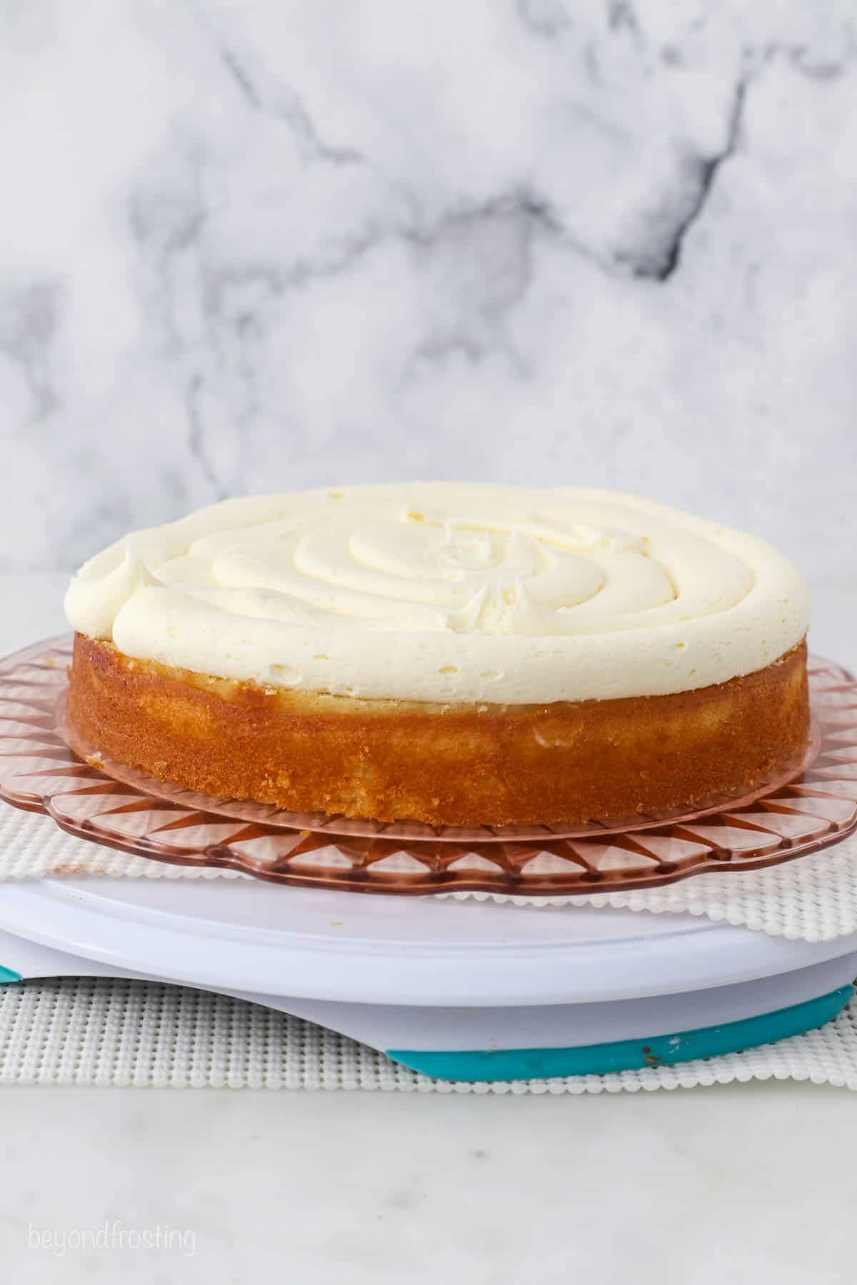 The first vanilla cake layer topped with an even layer of vanilla frosting.