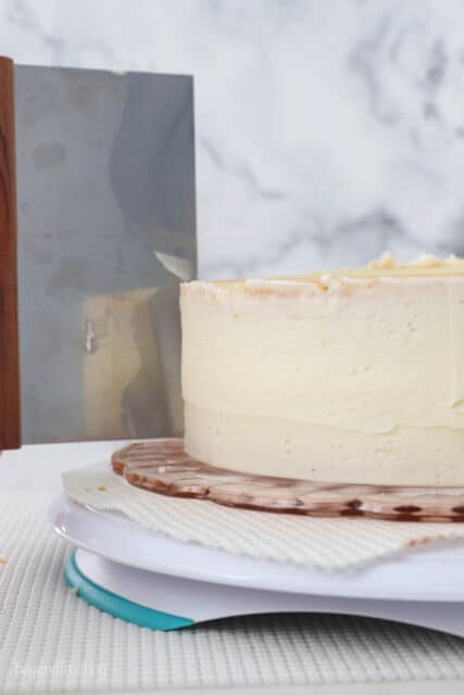 A cake scraper smoothes out the crumb coat on a double-layer cake.