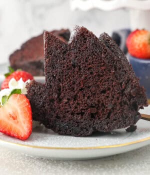 A slice of chocolate rum cake on a plate next to sliced strawberries and a swirl of whipped cream.