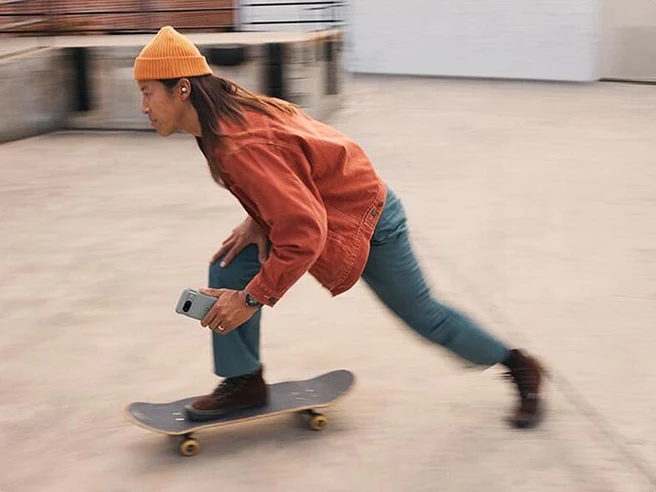 An individual riding on a skateboard with a Pixel 9 device in Moonstone color in their hand