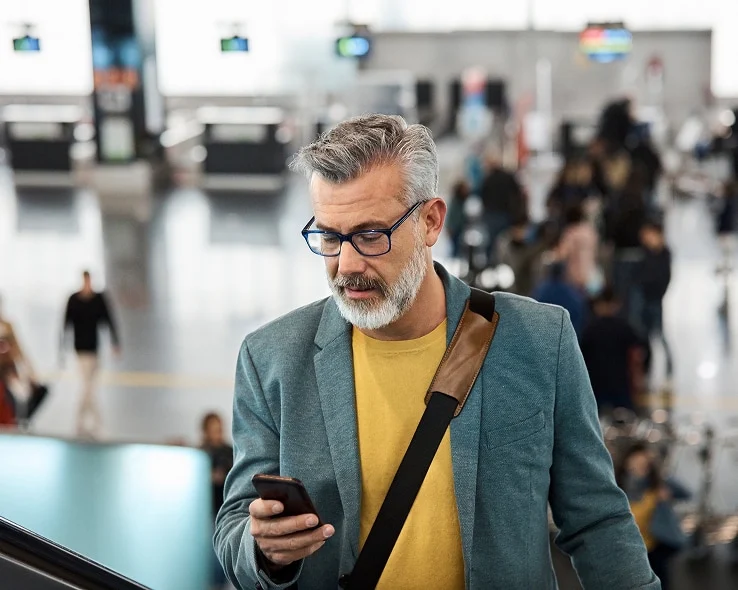An individual going up an escalator at an airport, looking at his device.