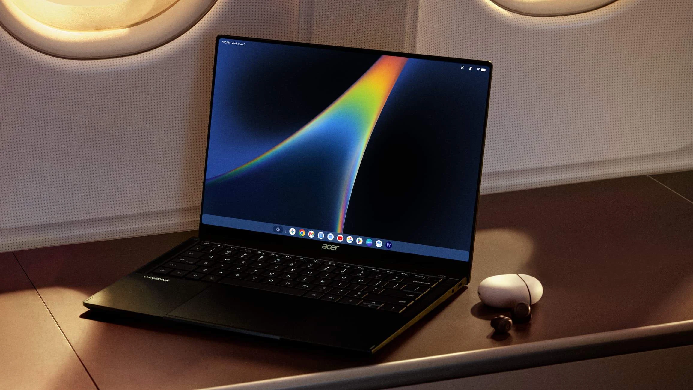 An open Acer Googlebook laptop, Google Pixel phone, and wireless earbuds sitting on an airplane tray table.