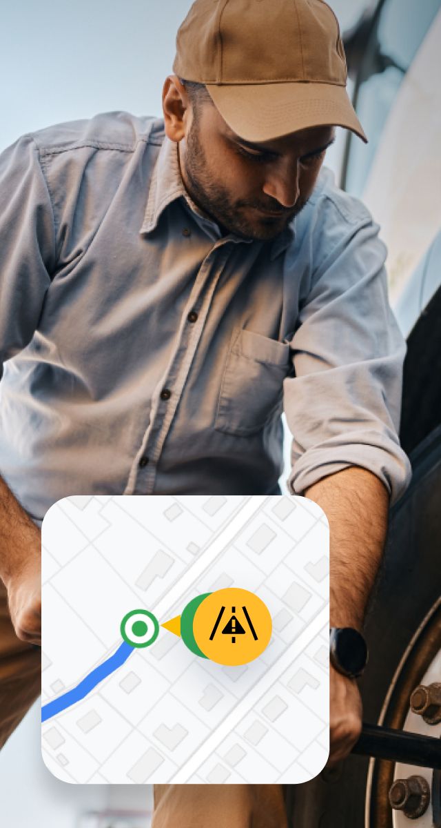 A man in a cap works on a vehicle tire with a map overlay showing a roadside assistance alert icon.