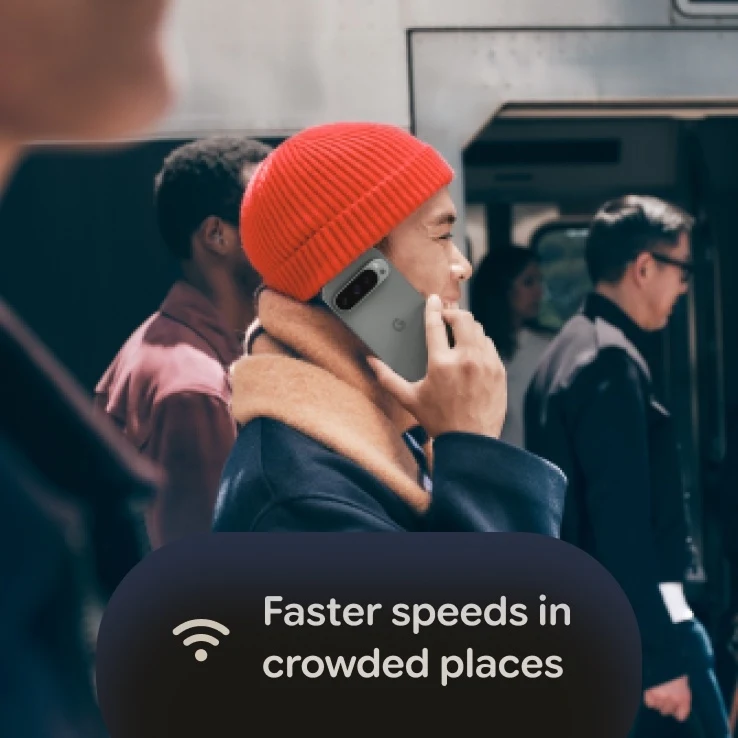 A man wearing a red beanie talking on a Google Pixel 11 Pro in Moonstone in a crowded area, with an overlay reading "Faster speeds in crowded places" with a Wi-Fi icon.