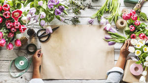 Hands crafting with tulips and floral supplies on a wooden table.