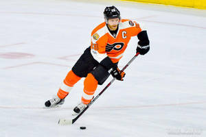 Hockeyspelare i orange och svart uniform åker med klubba på is.