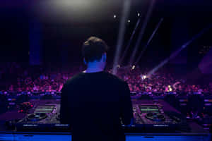 DJ performing at a lively nightclub with glowing equipment and cheering crowd. — Dj Picture