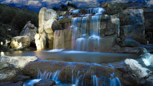 A glowing waterfall cascades over rocks under twilight skies with ambient lighting.