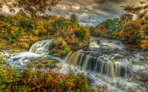 Autumn waterfall flowing through colorful forest under cloudy sky