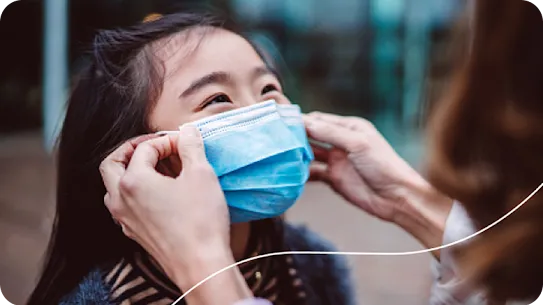 An adult gently places a surgical mask on a child's face.