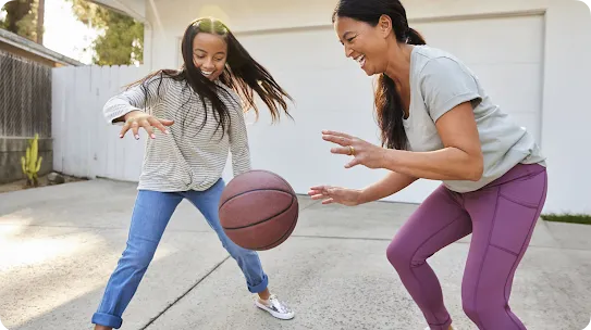 A woman and a young girl playing basketball together in a driveway.