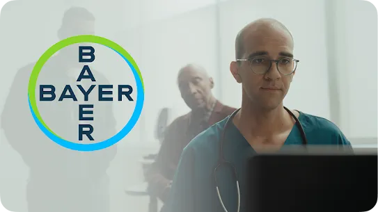 A doctor looks at a laptop with a patient behind them, with a faint Bayer logo visible.