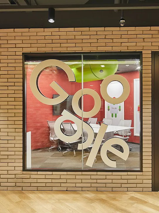Ein Besprechungsraum von außen. Auf dem Glasfenster ist das Google-Logo zu sehen.
